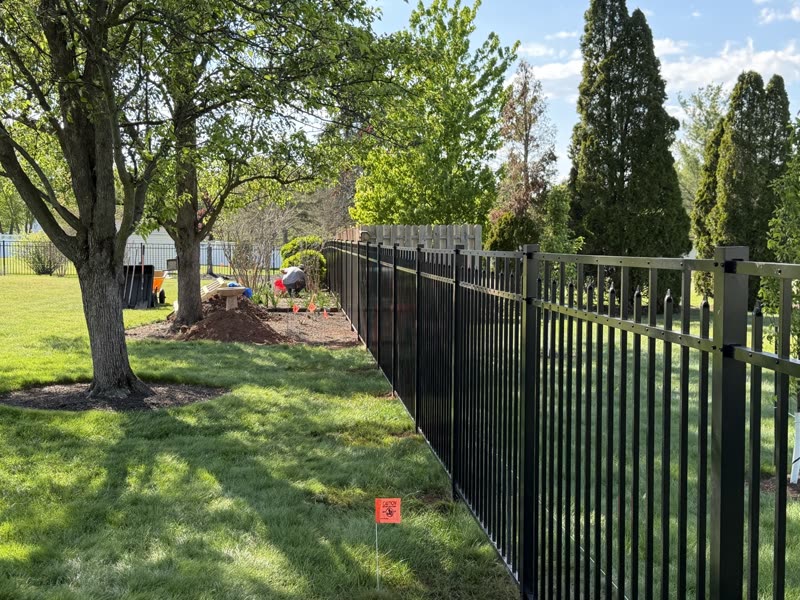 Black aluminum fence corner under trees with a new post set