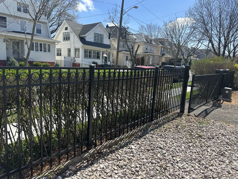 Black aluminum fence along a sidewalk with hedges