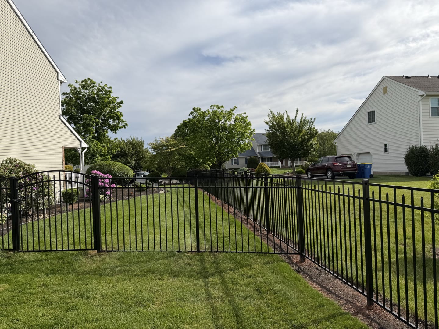 Black aluminum fence with an arched walk gate beside a home