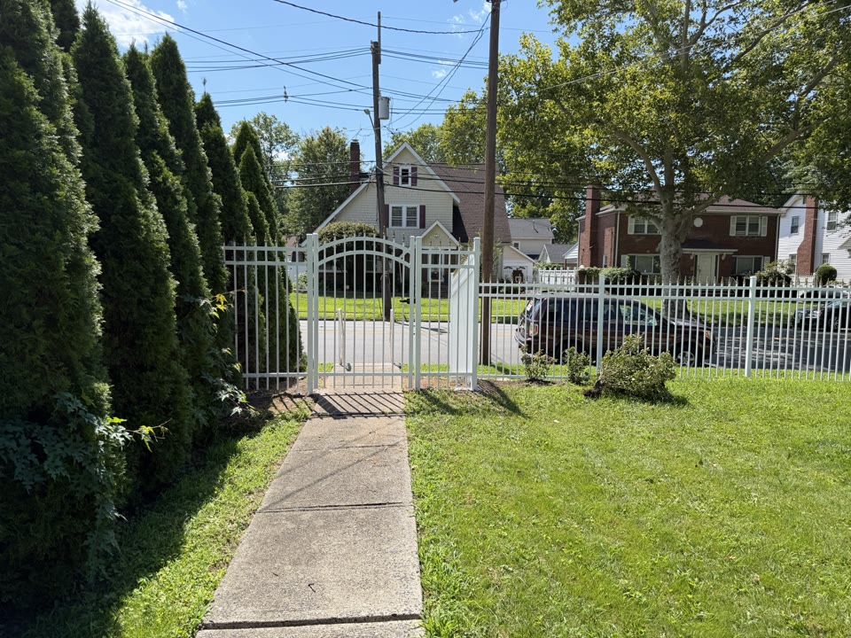White arched walk gate between tall cypress trees