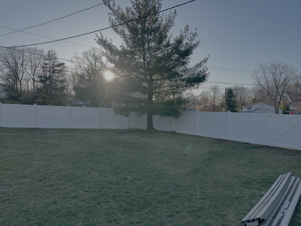 White vinyl privacy fence with the sun setting behind a tree